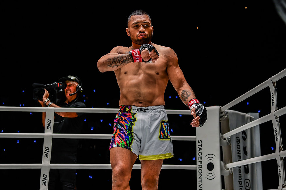 MMA fighter in colorful shorts in a ring, adjusts glove. Camera operator films nearby. Bright lights, focused expression.