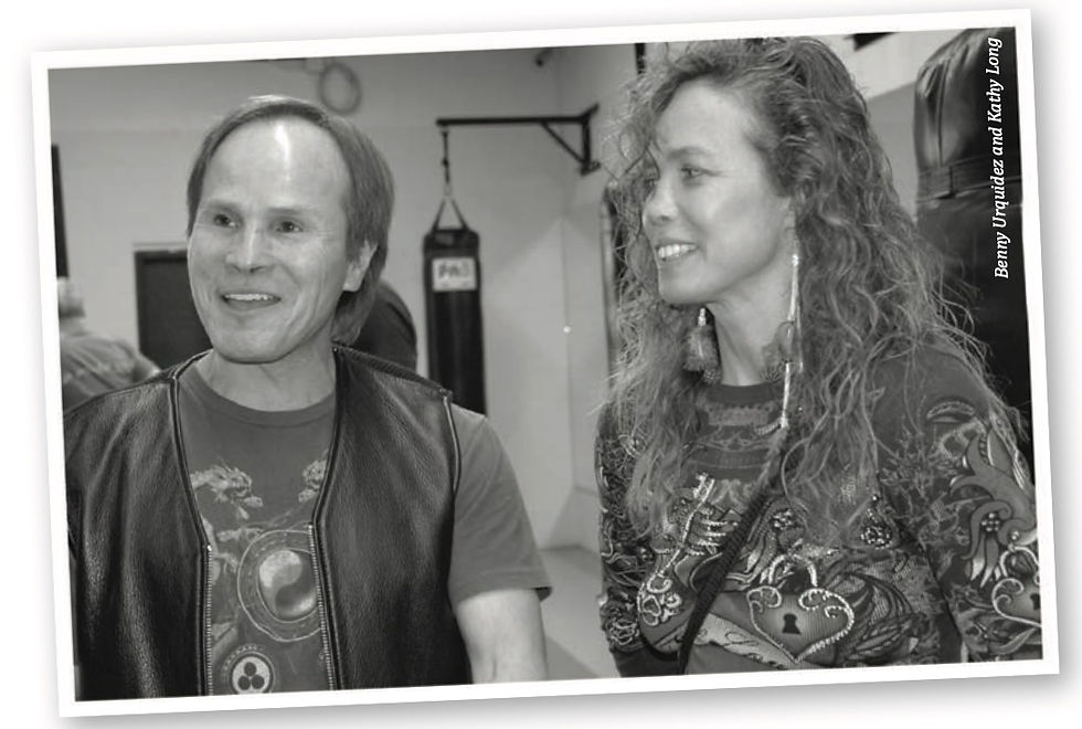 Smiling man and woman in a boxing gym, with a punching bag behind them; vertical text reads Benny Urquidez and Katy Long