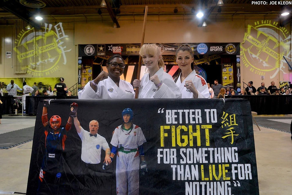 Three martial artists in white uniforms pose, smiling, behind a banner with "Better to fight for something than live for nothing" text. Event hall.