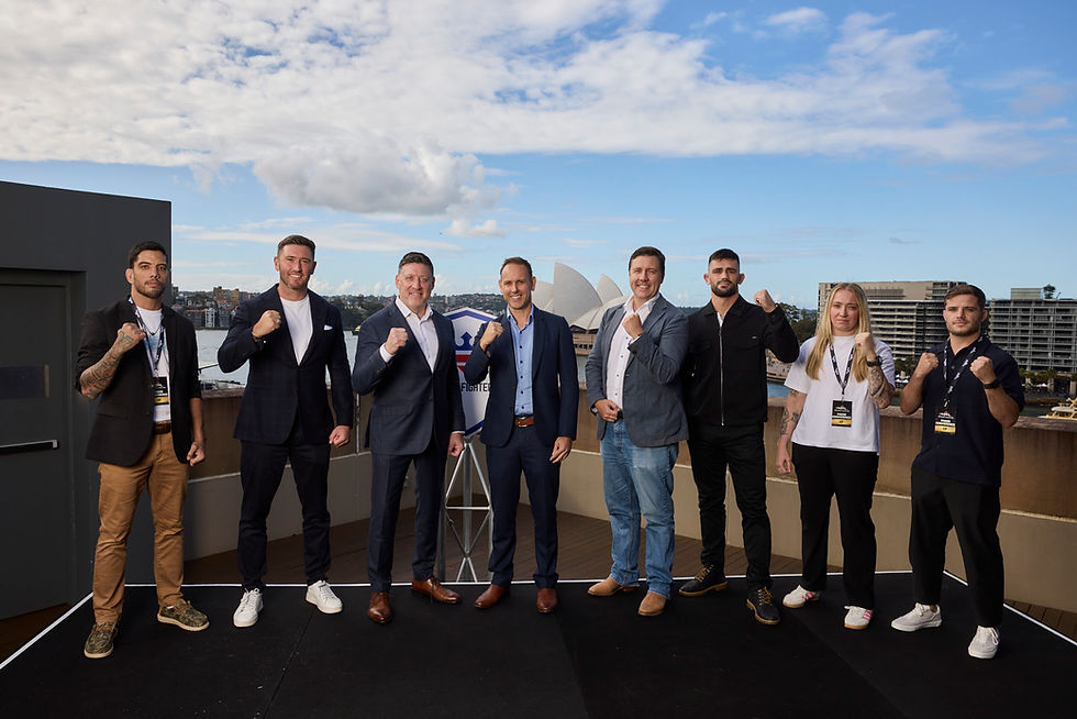 Eight people stand on a rooftop with fists raised. Sydney Opera House visible in the background, with a blue sky and scattered clouds.