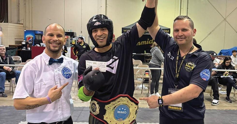Three men in an indoor sports venue, central figure in protective gear holding a check and wearing a WAKO championship belt, showing joy.