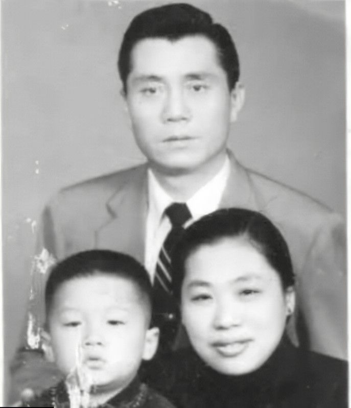A black and white photo of a family: a man in a suit, a woman, and a young child. All are facing forward with neutral expressions.