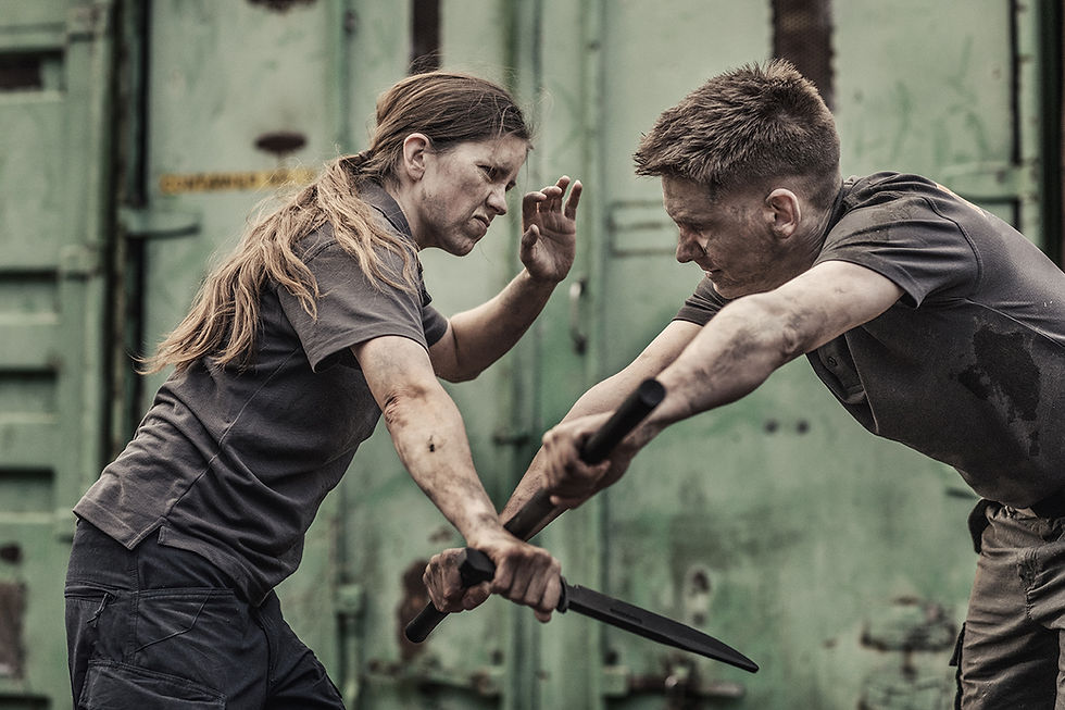 Two people engage in a knife fight, wearing dark clothing, against a green industrial background. Intense expressions, suggesting conflict.