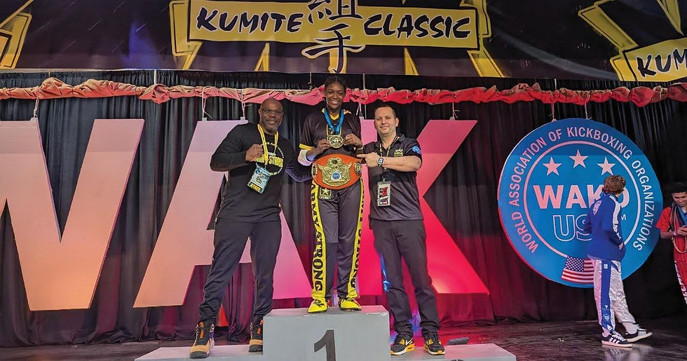 Three people on a podium, one holding a championship belt, celebrate at a kickboxing event. "Kumite Classic" and "WAKO" signs visible.