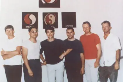 Six men standing in front of martial arts symbols on a wall, dressed casually. The mood is friendly and relaxed.
