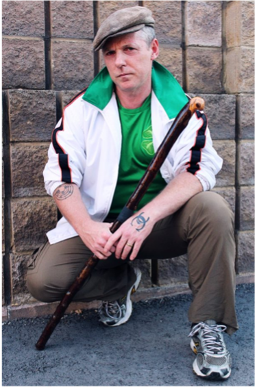 man poses against a wall with a fighting stick