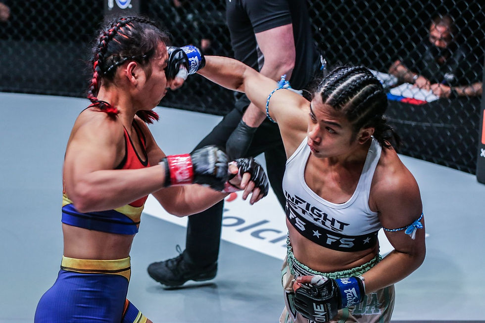 Two female fighters exchange punches in a caged ring. One wears a red and blue outfit, the other white and green. A referee and audience are visible.