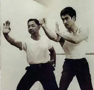 Two men in white shirts practice martial arts with focused expressions in a minimalistic setting.