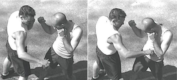 Two men sparring outdoors on grass, wearing sleeveless shirts and shorts. One man punches, the other defends. Black-and-white image.