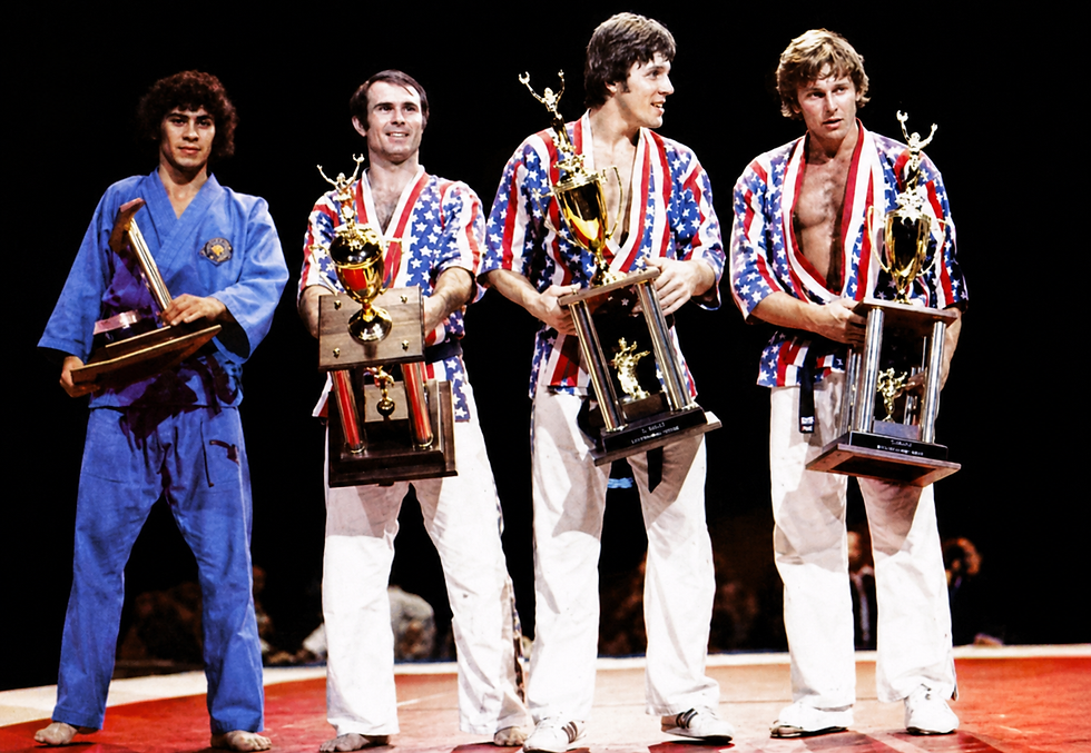 Four martial artists in blue and star-spangled uniforms hold trophies on a stage, posing proudly against a black backdrop.