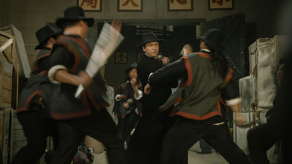 Men in black hats and black-red outfits fight in a dim room; one man blocks blows, with Chinese characters on the wall.