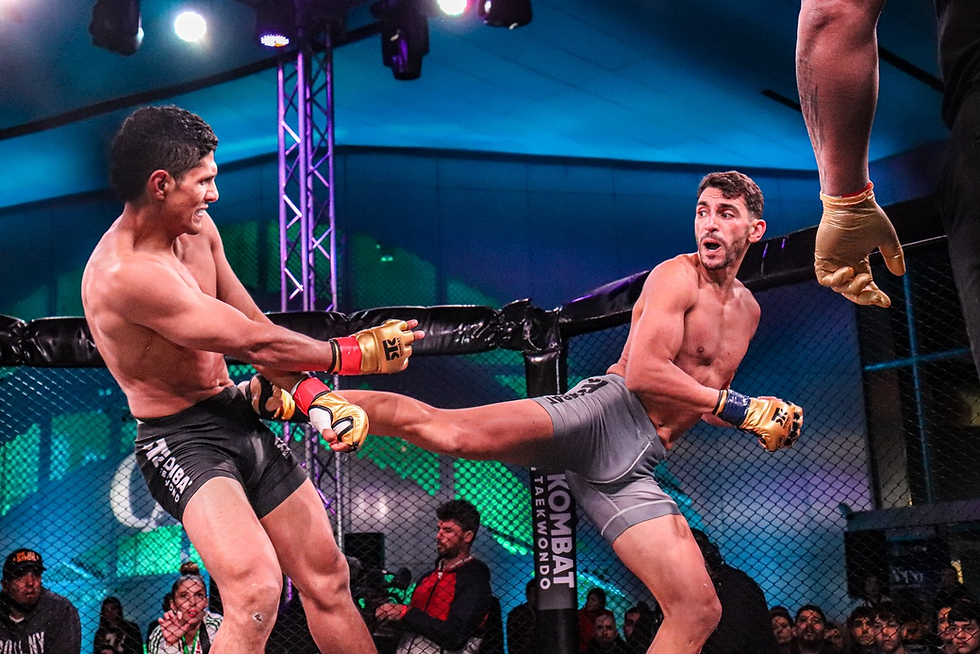 Two fighters in a cage match. One kicks the other, displaying intense expressions. Background is lit with blue and green lights. Text: "KOMBAT."