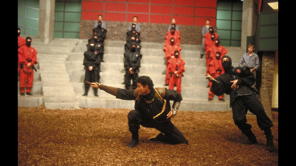 Martial artists in black outfits perform dynamic poses on a wood-chip floor, while spectators in red and gray uniforms watch from steps.