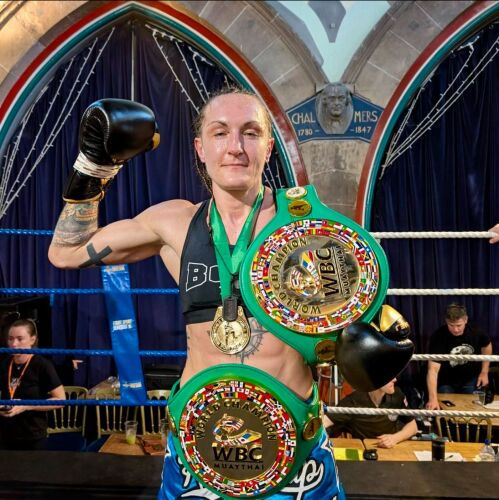 Boxer raising a fist, wearing a black tank top and blue shorts, adorned with multiple WBC title belts. Background features a decorated arch.